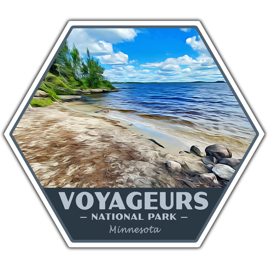 A hexagonal travel-style sticker featuring a painted beach shoreline by a lake under a blue sky, with the text 'VOYAGEURS NATIONAL PARK Minnesota' along the bottom.