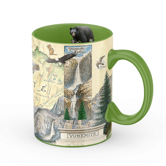 A ceramic mug featuring a Yosemite Falls map design with illustrated scenery, a small black bear perched on the rim, and a green handle and interior, shown on a white background.