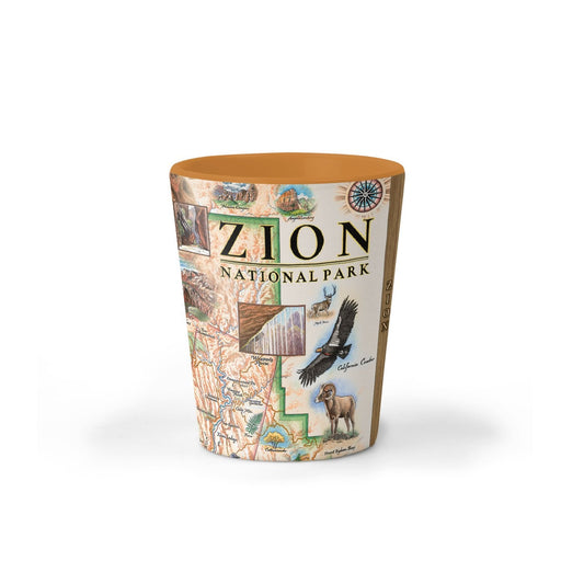 A cylindrical shot glass featuring a detailed illustration of Zion National Park, including a map, a desert landscape, a bison, and the text 'ZION NATIONAL PARK'. The shot glass has a warm brown rim and base, and is shown on a clean white background with a soft shadow.