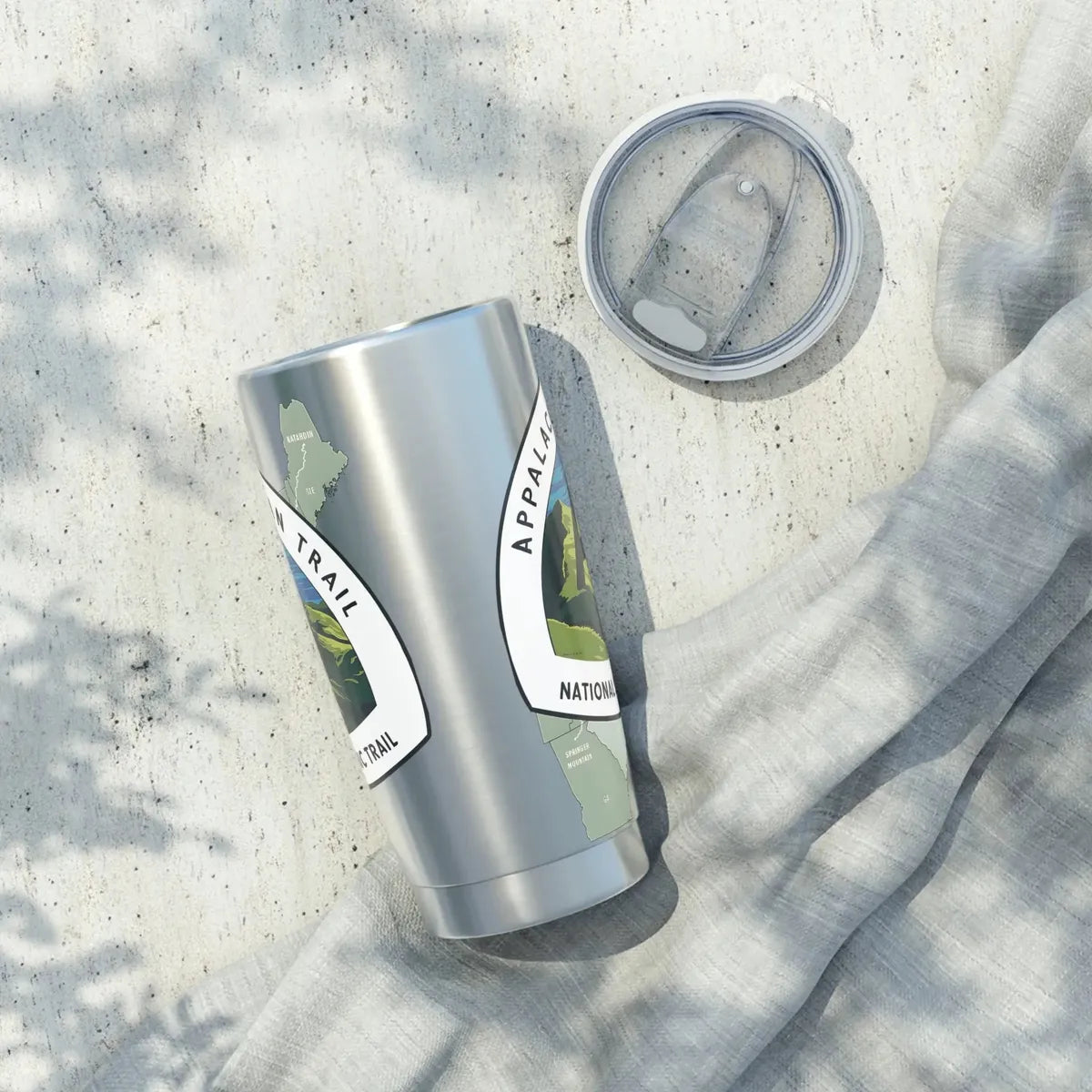 Stainless steel tumbler with Appalachian trail logo and map design laying on a concrete surface.