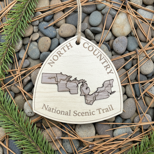 North Country Ornament laying on a bed of River rock with Pine needles and pine boughs.