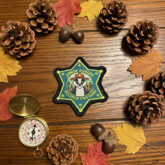 Star badge shaped embroidered patch with a badger wearing a ranger hat and the text “Junior Ranger Wisconsin State Parks” on a wood table top with decorative elements.