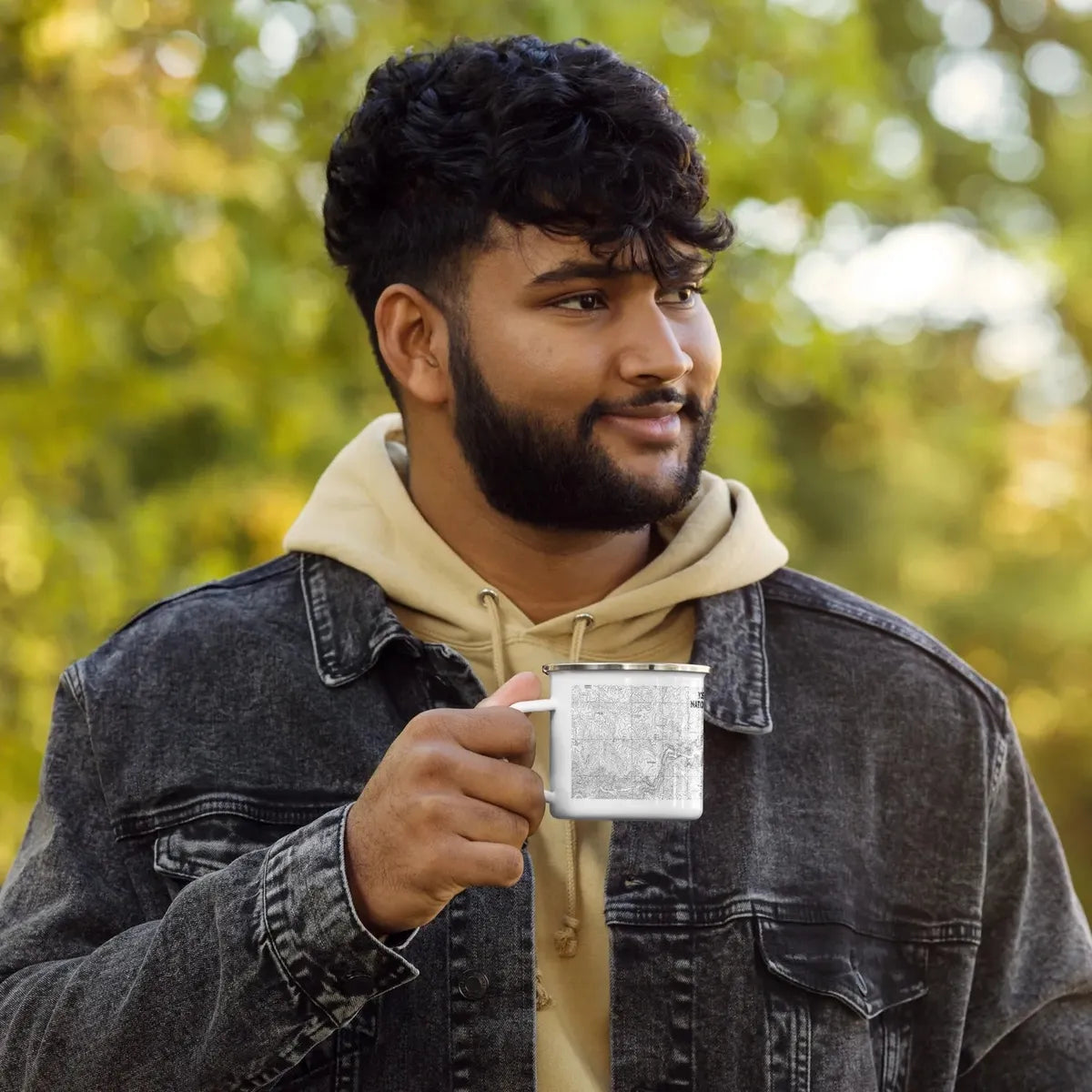 Male individual holding a white topographical, Yosemite national Park enamel camping mug in the woods